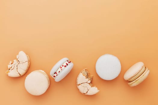 White, yellow, gold macaron cookies. Colorful, sweet small French macaroon cakes laying on the table. Light yellow-beige background. Broken cut, bitten parts, halves. High quality photo