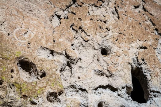 An ancient dwelling in the cliff face surrounded by petroglyphs in Bandelier National Monument, New Mexico