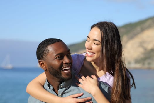 Happy interracial couple laughing on the beach on summer vacation