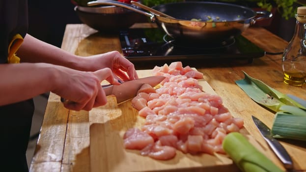Woman slicing meat for cooking on kitchen table. Closeup hands. Cosy dark room. Real, authentic cooking.