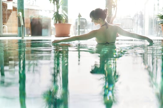 Wellness - white woman in her 30s enjoying water in pool, smiling.