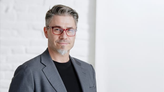 Portrait of happy good looking older businessman in glasses wearing jacket, smiling in front of white background with copy space. .