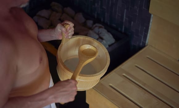 Real, authentic sauna moment. Man sweating in hot sauna, holding sauna bucket making steam.