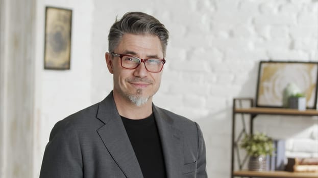 Portrait of happy good looking older businessman in glasses wearing jacket, smiling in front of casual home indoor.