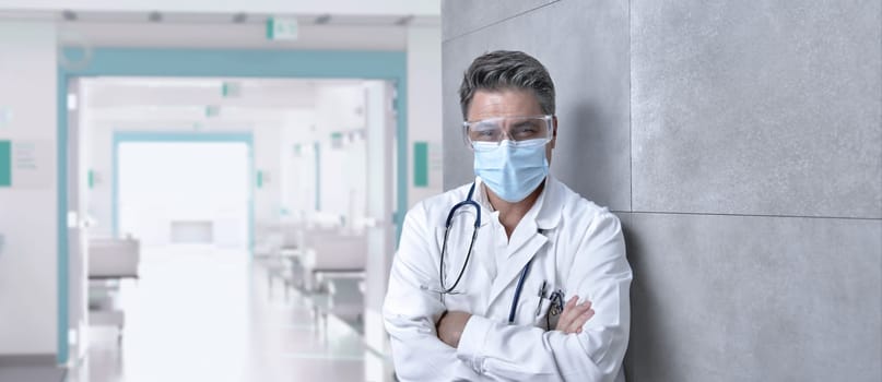 Covid-19 - Smiling doctor in glasses on hospital corridor, Trustworthy older man with gray hair.