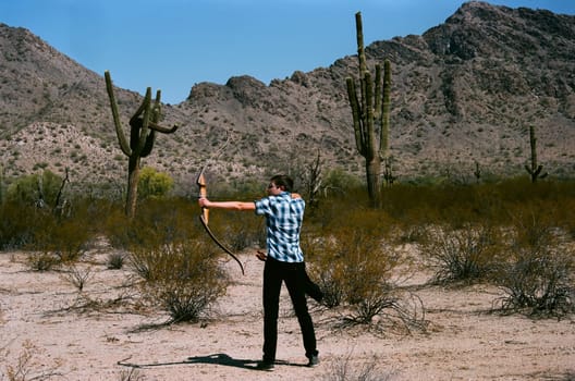 Young man shooting a bow and arrow in the desert