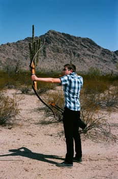 Young man shooting a bow and arrow in the desert