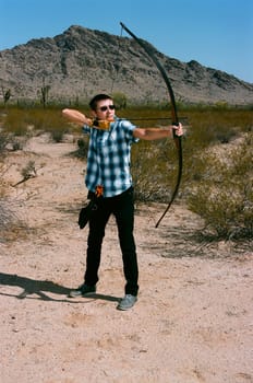 Young man shooting a bow and arrow in the desert