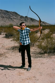 Young man shooting a bow and arrow in the desert