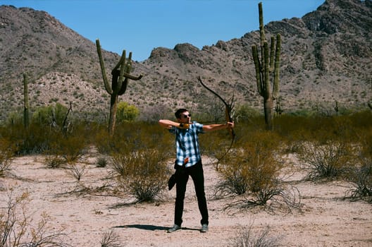 Young man shooting a bow and arrow in the desert