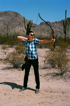 Young man shooting a bow and arrow in the desert