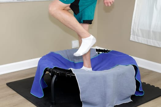 Adult male legs jogging on a round black rebounder covered with two workout towels. Left side view of legs of an adult white male exercising on a black round rebounder that has two workout towels.