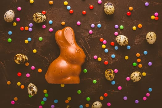 Delicious chocolate easter eggs, bunny and sweets on dark brown background