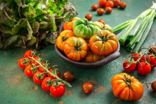 Assortment of tomatoes, lettuce and sprin onions on green background
