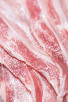 Close up top view pack bacon, pieces raw meat of fresh red pork with white fat slices are sliced into thin strips stacked on top of each other