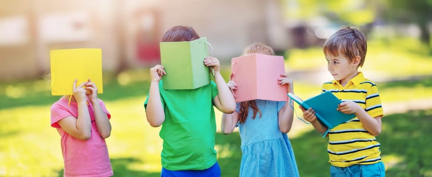Children standing in the park covered faces with books. Concept of the studying, learning, reading and friendship.