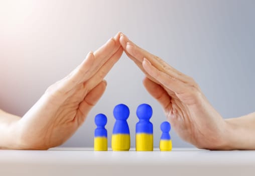 Woman hands under wooden models of family painting in colours of Ukrainian flag. The concept of helping the people of Ukraine running away from the war.