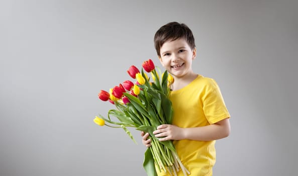 Cute boy standing indoors with bouquet of the colourful tulips. Concept of the Mother's day and family relationship.