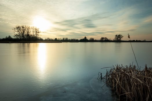 Beautiful sunset over a frozen lake with reeds, Stankow, Poland