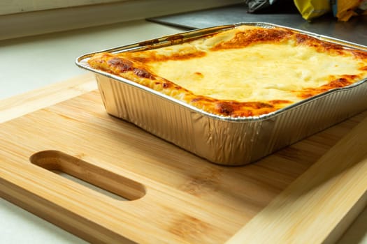 Delicious baked lasagne in an aluminum bowl on a wooden board