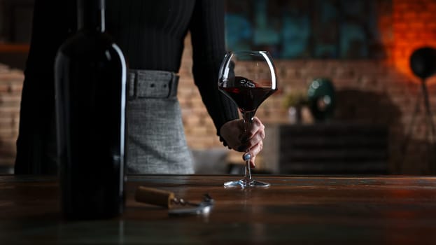Woman tasting and drinking red wine from wine from elegant wine glass at home in a cosy dark room.