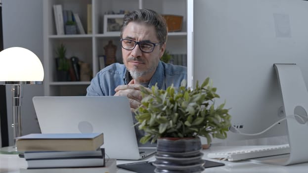 50s businessman with gray hair working from home. Man in casual sitting at desk using laptop computer, business manager online in home office.