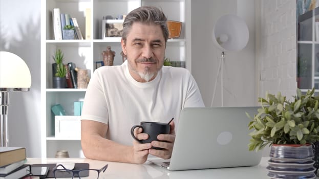 50s businessman with gray hair working from home. Man in casual sitting at desk using laptop computer, business manager online in home office.