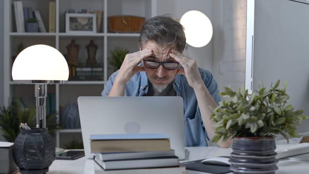 Older man working online with laptop computer at home sitting at desk. Home office, surfing internet, study room.