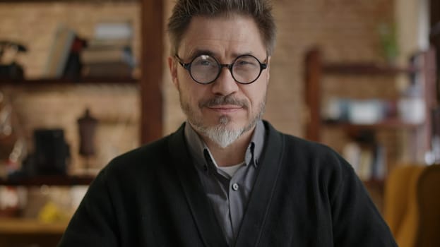Happy bearded older man at home wearing glasses looking at camera, smiling. Portrait of mature age, middle age, mid adult man in 50s.