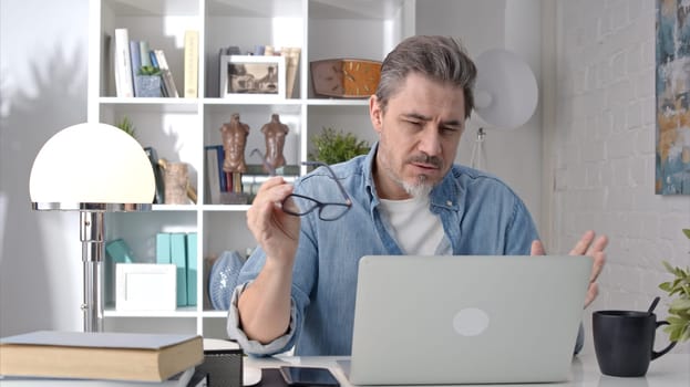 Older white man sitting at desk using laptop in home office. 50s businessman on video chat conference call and working from home.