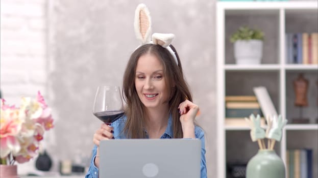 Happy woman talking and waving on video chat at home. Celebrating Easter online wearing bunny ears using laptop for video call.