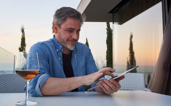 Happy man working online with tablet computer on terrace. Businessman in home office, browsing internet, tele working, video chat.