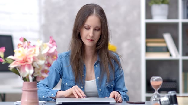 Young woman working online with laptop computer at home sitting at desk. Businesswoman in home office, browsing internet.