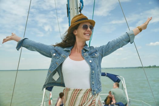 Happy young woman relaxing on sailing boat enjoying summer vacation. Wind, hat, sunglasses, traveling.