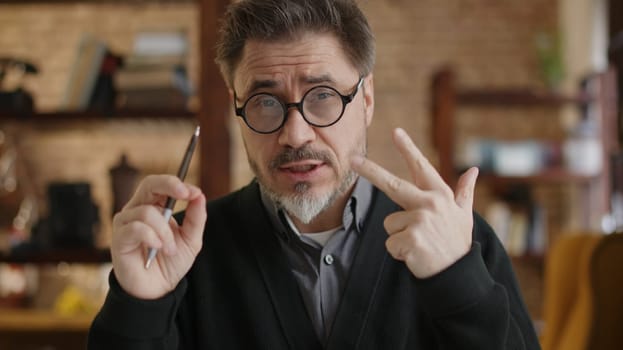 Teacher teaching online from home. Man wearing eyeglasses talking on conference call, explaining in E learning online class, lesson, training course. Mature, middle age, mid adult in 50s.