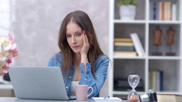 Young woman working online with laptop computer at home sitting at desk. Businesswoman in home office, browsing internet.