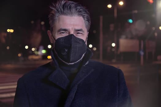 Covid-19 portrait - man in medical face mask on street in Winter. City lights at night.