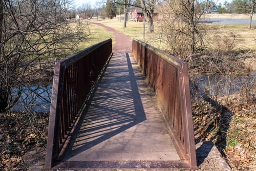 Shot from the end of the sturdy red bridge this image has new journey fresh start concepts as the hiking trail extends into the distance through a pennsylvania country landscape with green grass. No people, with copy space.