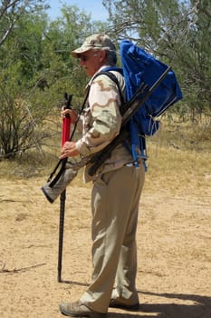 Senior hunter in sonora desert carrying rifle and pack