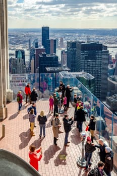 People tourists on the observation deck of Rockefeller Center, view from high angle, New York City with lots of skyscrapers and Hudson river in the background, vertical