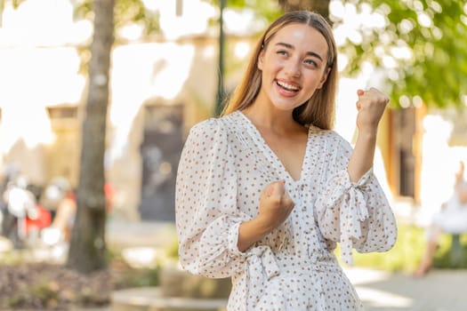 Excited happy woman traveler shouting, celebrating success, winning, goal achievement, good news, lottery jackpot luck, victory outdoors. Young lady standing on urban city sunshine street. Lifestyles