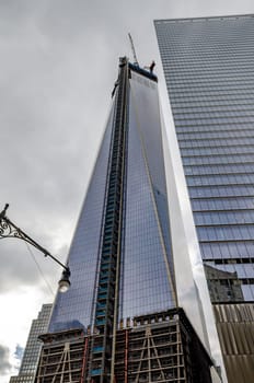 One World Trade Center construction area with crane on top during daytime with overcast, New York City, view from low angle, vertical