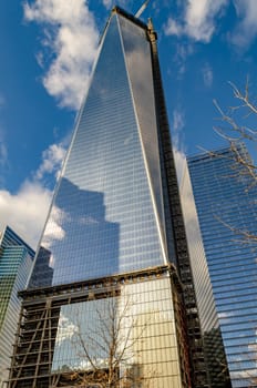 One World Trade Center construction area with  clouds reflection in the window, crane on top during daytime with overcast, New York City, view from low angle, vertical