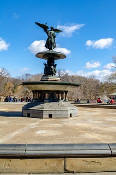 Bethesda Fountain with Angel of the Waters Sculpture, close-up, front view from low angle, Central Park New York during winter, birds sitting on the wing of the angel, people in the background, clear sky, vertical