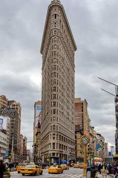 Flatiron Building New York City with street and crosswalks, yellow taxi cabs in forefront during daytime with overcast, view from low angle, vertical