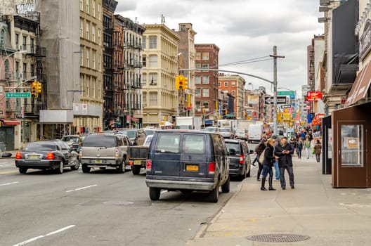 Brooklyn, New York City wide Street with lots of traffic, red traffic light, delivery vehicles and lots of cars on the street, people walking on the sidewalk, overcast in the evening, horizontal