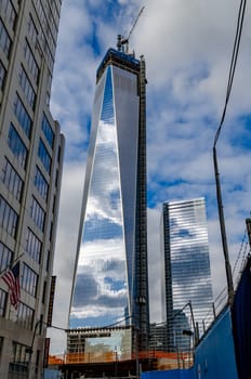 One World Trade Center construction area with  clouds reflection in the window, crane on top during daytime with overcast, New York City, view from low angle, vertical