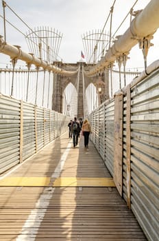 People walking on Brooklyn Bridge during sunset, New York City, rear view, construction area on the bridge, vertical