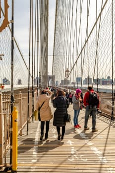 People walking and standing on Brooklyn Bridge during sunset, New York City, construction area on the bridge, vertical