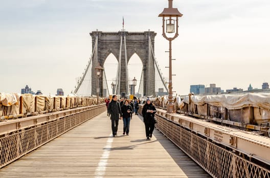 People walking on Brooklyn Bridge, New York City in the evening, street lamp in forefront, clear sky, construction area on the bridge, horizontal
